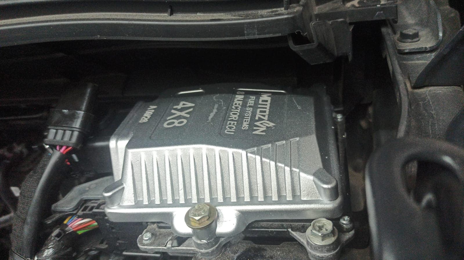 CNG ECU bolted in an engine bay, with its wiring harness connected